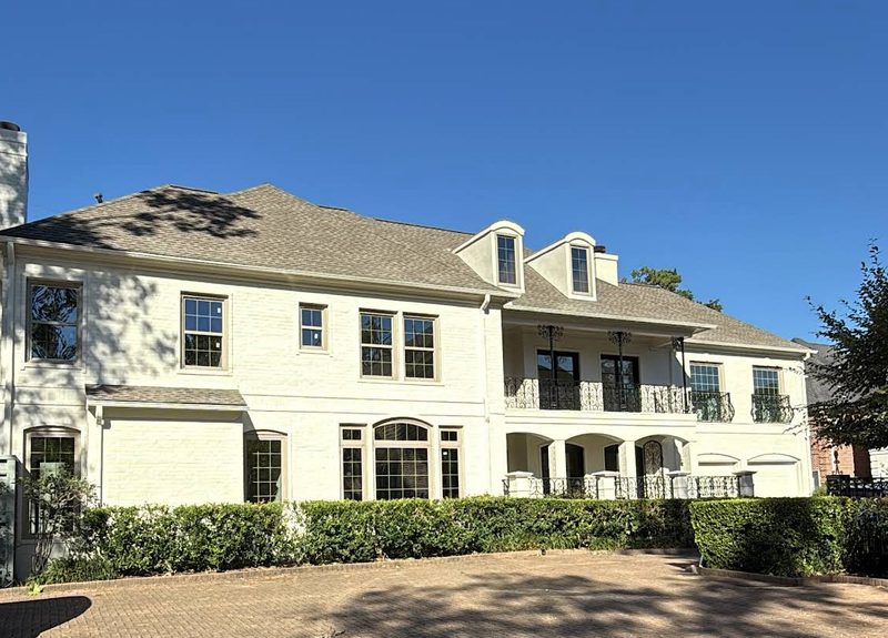 White brick two-story home with a new shingle roof and new windows by Built by Revitalize